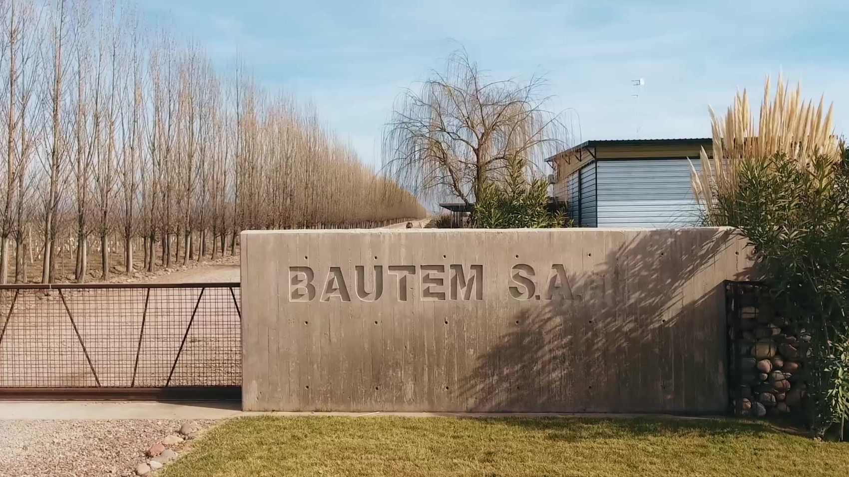 La entrada a Finca Bautem, con el muro de hormigón y la alameda